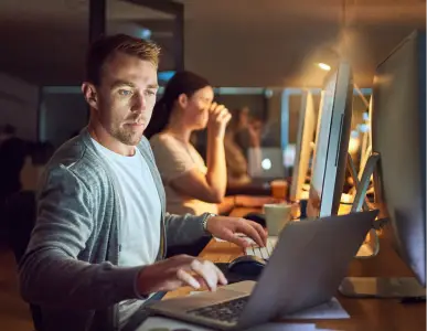 A man working on two computers to help a team with the resource augmentation